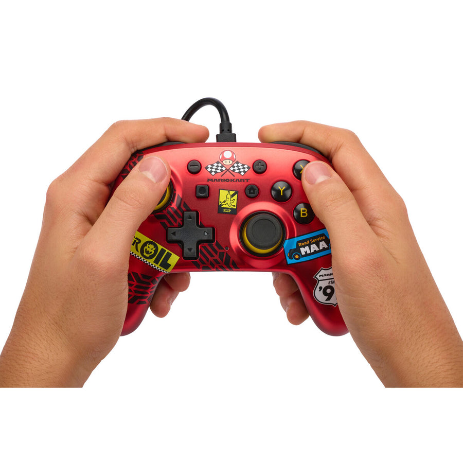 Hands holding a red wired Powera NSGP0124-01 gaming controller with USB connection and plug-and-play functionality.